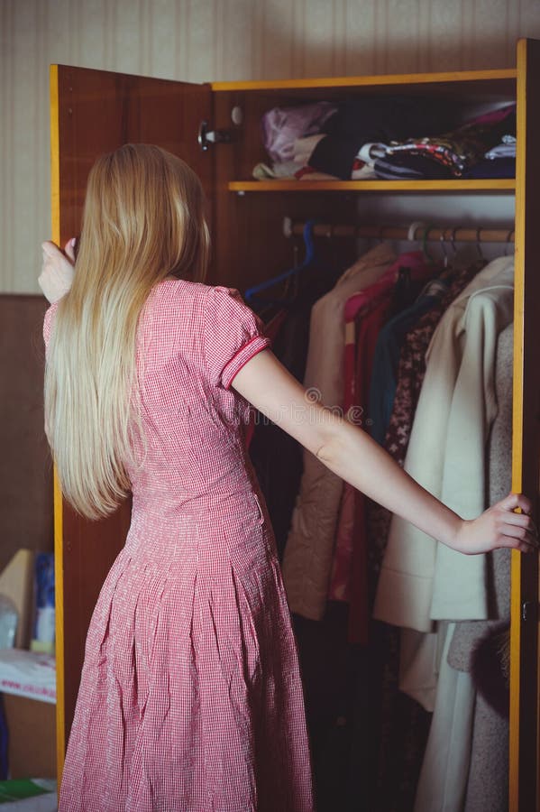 Blonde woman looks in a closet, dressed in a red dress, stands in an old house, a simple home image.  royalty free stock photo