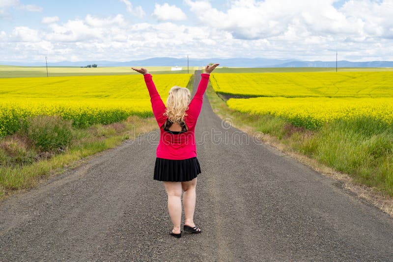 Blonde woman poses on an empty farm road with arms raised, near a field of mustard flowers in the Palouse region of Western Idaho stock image Blonde woman poses on an empty farm road with arms raised, near a field of mustard flowers in the Palouse region of Western Idaho stock image