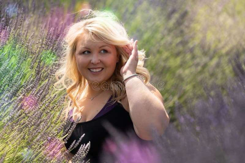 Blonde woman sits in a lavender field, looking off to the side, pushing hair out of her face stock images Blonde woman sits in a lavender field, looking off to the side, pushing hair out of her face stock images