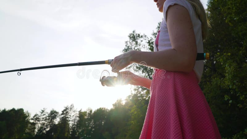 Blonde young girl fisherman is fishing on the forest lake, holding the fishing rod twists the coil. woman in short