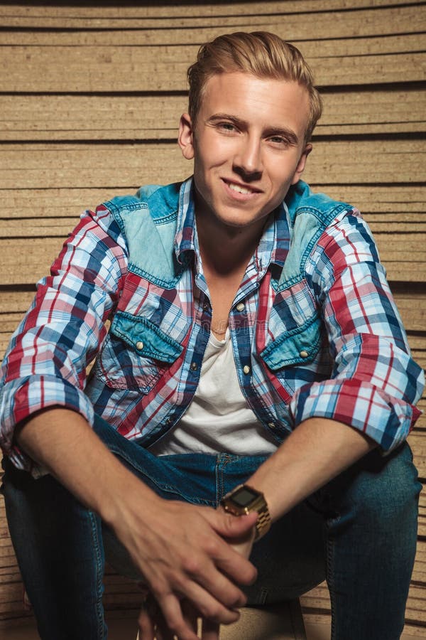 Portrait of blonde young man sitting in studio while smiling at the camera