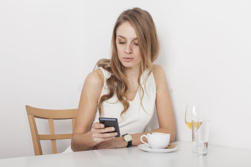 Blonder Stirring ihr Kaffee, der Handy betrachtet stockfoto Blonder Stirring ihr Kaffee, der Handy betrachtet stockfoto