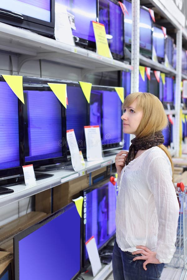 Blondes Mädchen betrachtet Plasma Fernsehapparate im Supermarkt lizenzfreie stockfotos Blondes Mädchen betrachtet Plasma Fernsehapparate im Supermarkt lizenzfreie stockfotos