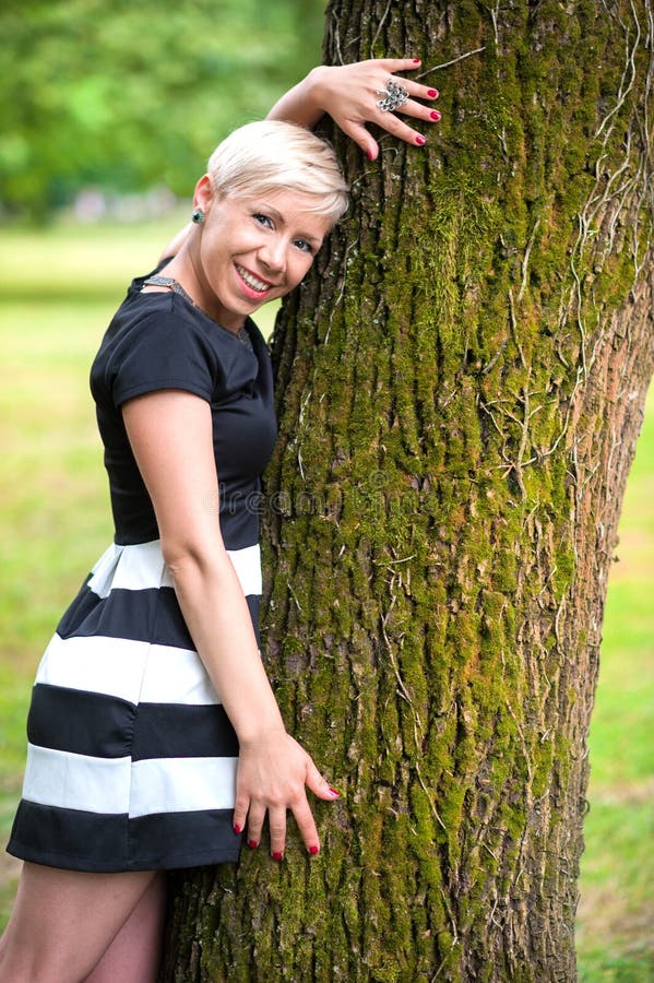 Cute girl with blonde hair in black and white dress hug the tree. Cute girl with blonde hair in black and white dress hug the tree