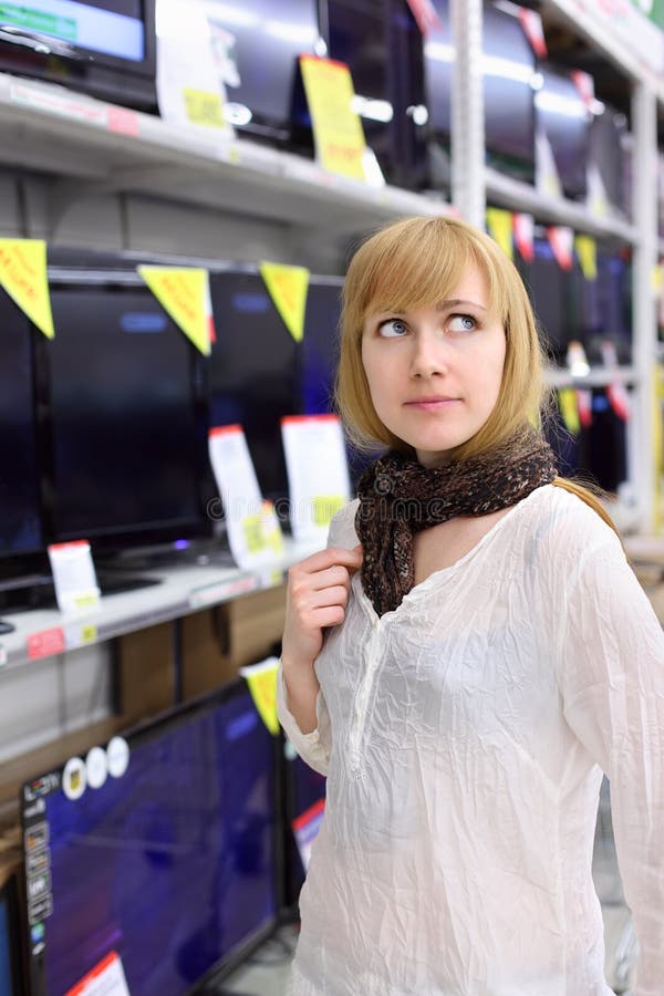 Blondes Mädchen denkt an das Kaufen von Fernsehapparat im Supermarkt lizenzfreies stockbild Blondes Mädchen denkt an das Kaufen von Fernsehapparat im Supermarkt lizenzfreies stockbild