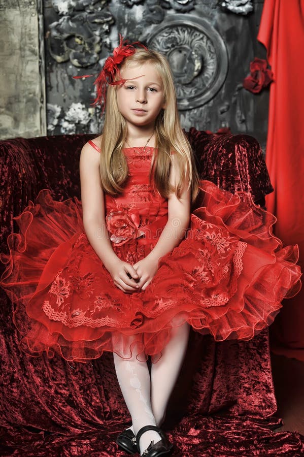 Blonde girl in a red elegant dress with a red hairpin in her hair sitting on an armchair, retro style. Blonde girl in a red elegant dress with a red hairpin in her hair sitting on an armchair, retro style