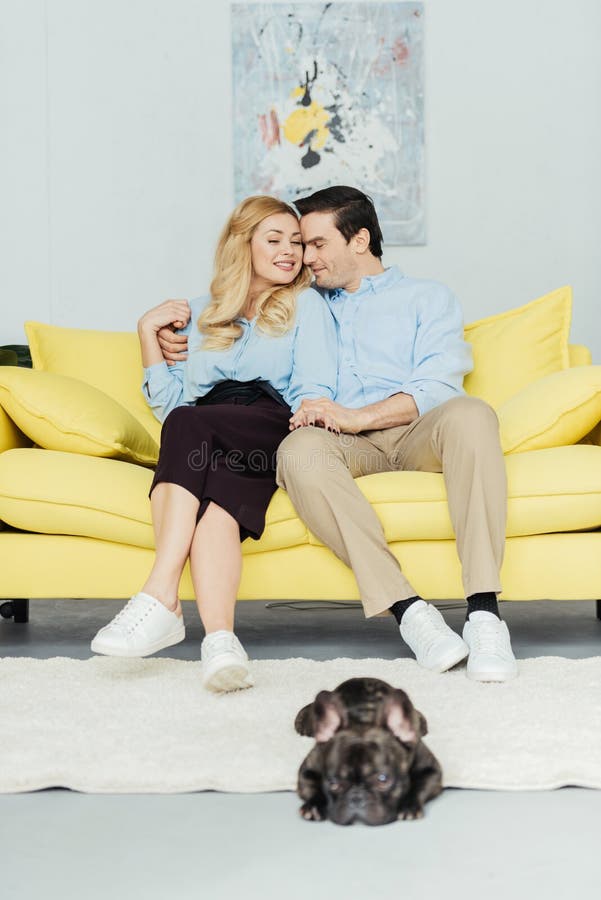 Blondevrouw die haar vriend op bank door Franse buldog koesteren stock afbeeldingen Blondevrouw die haar vriend op bank door Franse buldog koesteren stock afbeeldingen