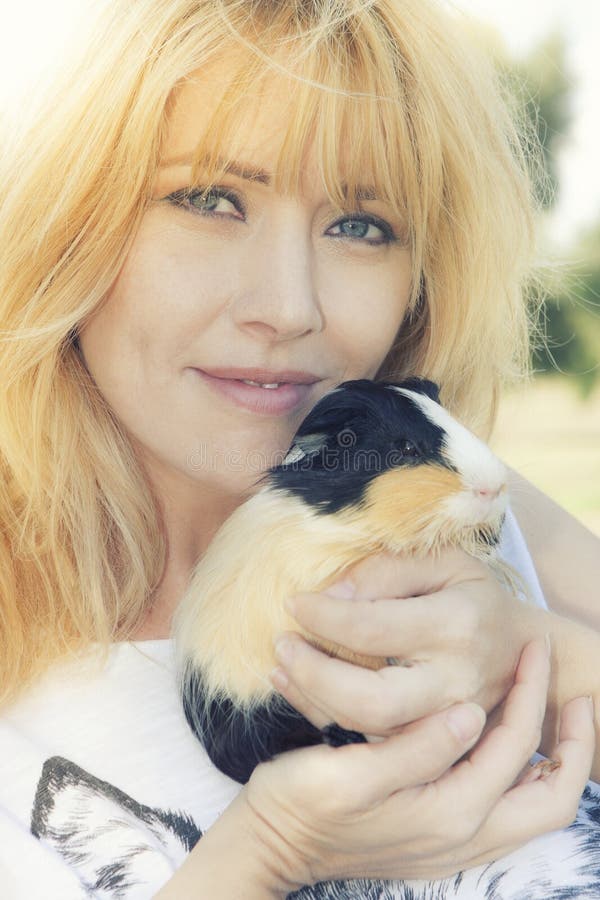 A beautiful Italian woman with blond hair is hugging a puppy Peruvian guinea pig. Close portrait. A warm sun behind her and her hair. A beautiful Italian woman with blond hair is hugging a puppy Peruvian guinea pig. Close portrait. A warm sun behind her and her hair.