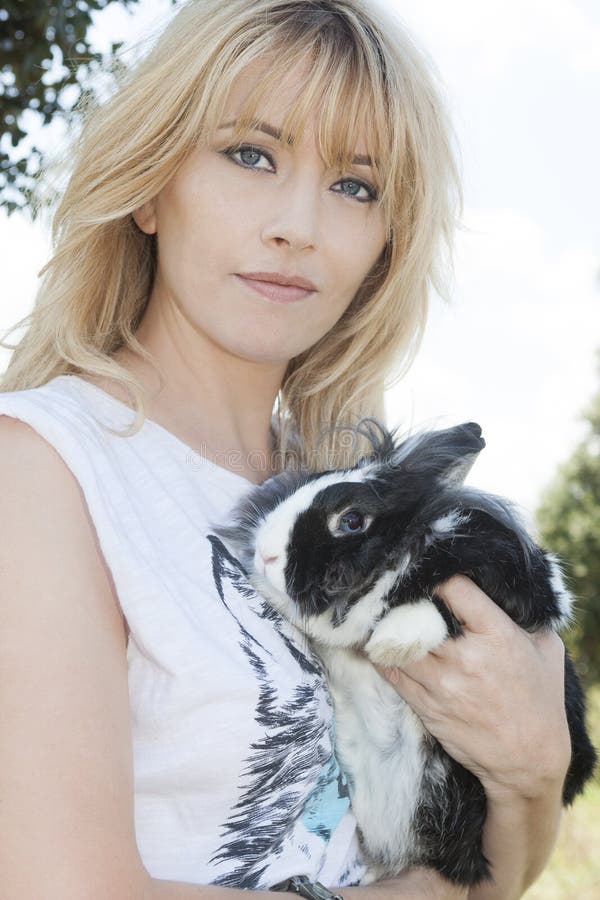 A beautiful Italian woman with blond hair is hugging a rabbit bunny. Close portrait. An intense light behind her and her hair. A beautiful Italian woman with blond hair is hugging a rabbit bunny. Close portrait. An intense light behind her and her hair.