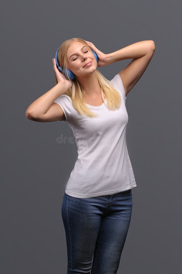 Young girl blonde in blue headphones. Listening, enjoying music. Isolate on gray background. Young girl blonde in blue headphones. Listening, enjoying music. Isolate on gray background.