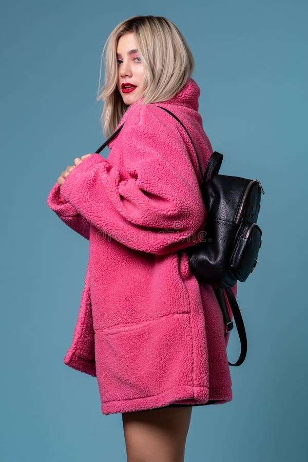 Blondynki rozochocona dziewczyna pozuje w eleganckim menchia żakiecie w studiu z czarnym plecakiem fotografia stock Blondynki rozochocona dziewczyna pozuje w eleganckim menchia żakiecie w studiu z czarnym plecakiem fotografia stock