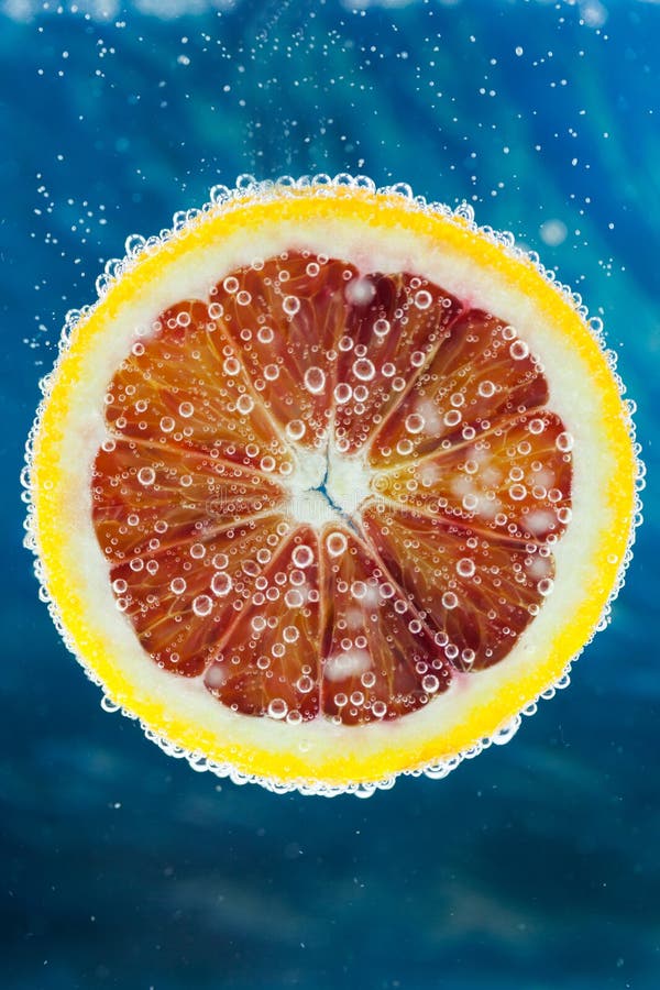 Blood orange slice falling into water. Sparkling, droplets.