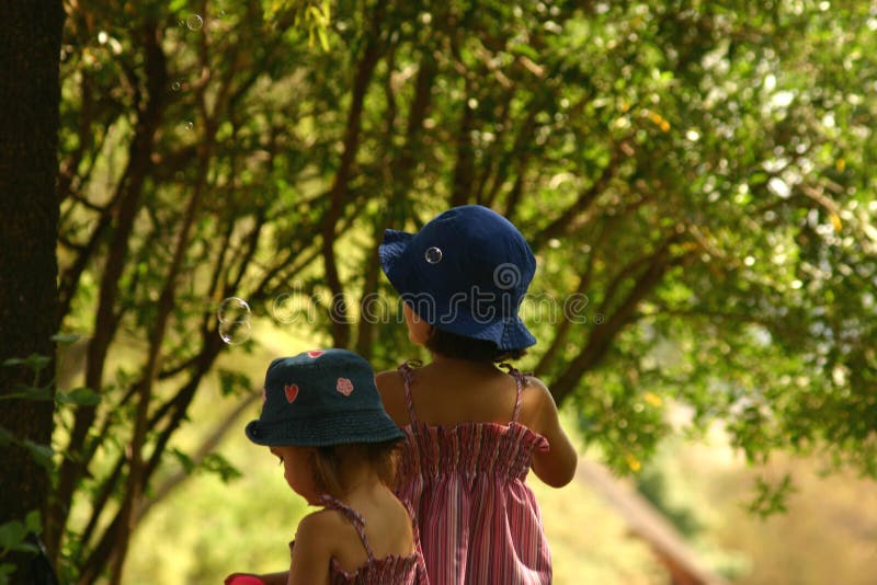 Two little blonds blowing bubbles in park