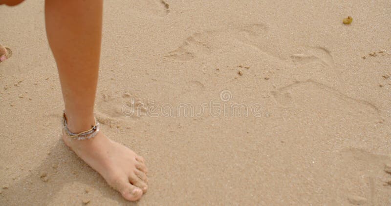 Bloße Füße beschichtet im Sand, der auf Strand geht