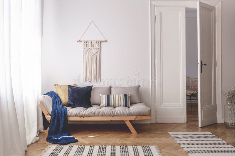 Blue blanket and pillows on wooden couch in white living room interior with rugs and door. Real photo