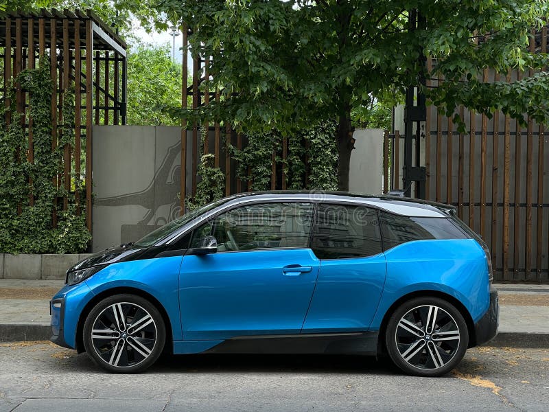 Blue BMW i3 stands near the sidewalk against the background of green trees. High quality photo