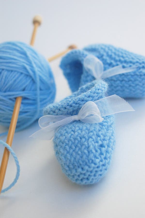 Blue booties with little bows, blue yarn and bamboo knitting needles photographed against a white background. Blue booties with little bows, blue yarn and bamboo knitting needles photographed against a white background