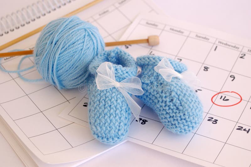 Blue baby booties, yarn and knitting needles resting on calendar, date circled in red. Blue baby booties, yarn and knitting needles resting on calendar, date circled in red