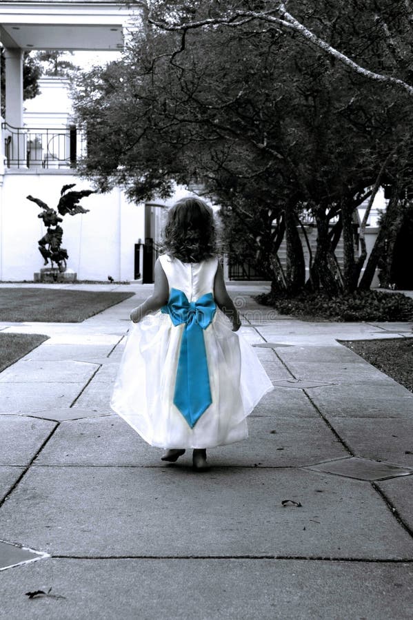 Little Girl skips through the park. She is wearing a white long dress with a bright blue bow. Photo is black and white. Little Girl skips through the park. She is wearing a white long dress with a bright blue bow. Photo is black and white.