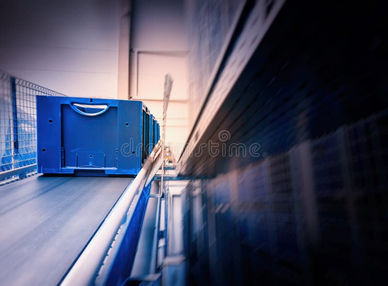 Blue boxes in a large, fully automated logistics warehouse run on a conveyor belt. Background is blurred. It is a modern storage system