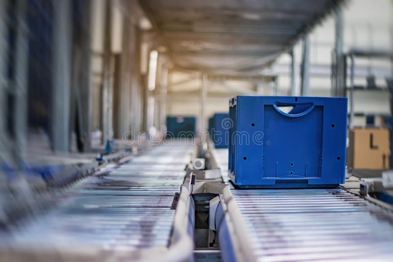 Blue boxes in a large, fully automated logistics warehouse run on a conveyor belt. Background is blurred. It is a modern storage system