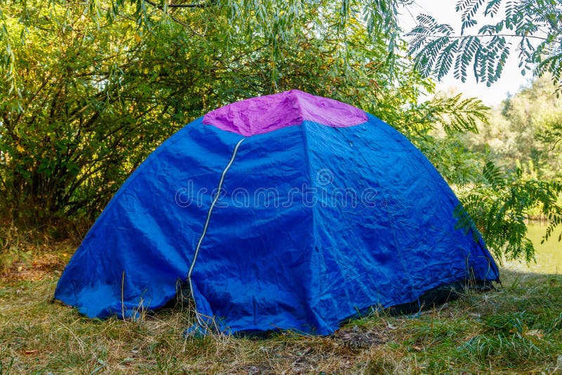 Blue Camping Tent and Backpack in Forest Near a River Stock Image