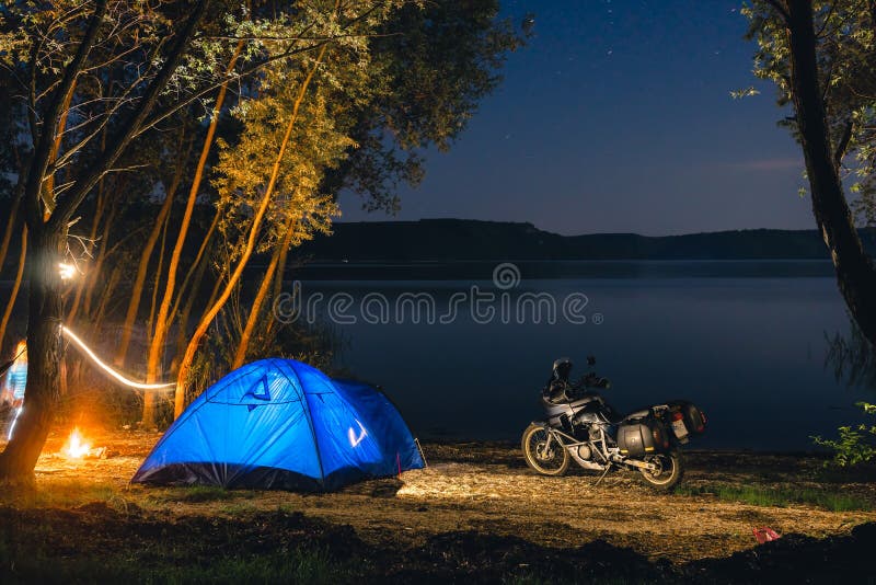 Blue Camping Tent Illuminated Inside. Night Hours Campsite. Recreation. Motorcycle traveler, tourist bikers. lake and stars. take royalty free stock photo Blue Camping Tent Illuminated Inside. Night Hours Campsite. Recreation. Motorcycle traveler, tourist bikers. lake and stars. take royalty free stock photo