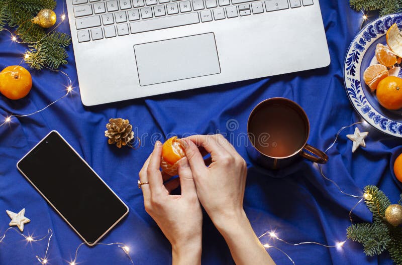 Blue Christmas New Year flat lay on the bed blanket with the laptop keyboard and a phone. Womans hands are peeling a tangerine. royalty free stock photography Blue Christmas New Year flat lay on the bed blanket with the laptop keyboard and a phone. Womans hands are peeling a tangerine. royalty free stock photography
