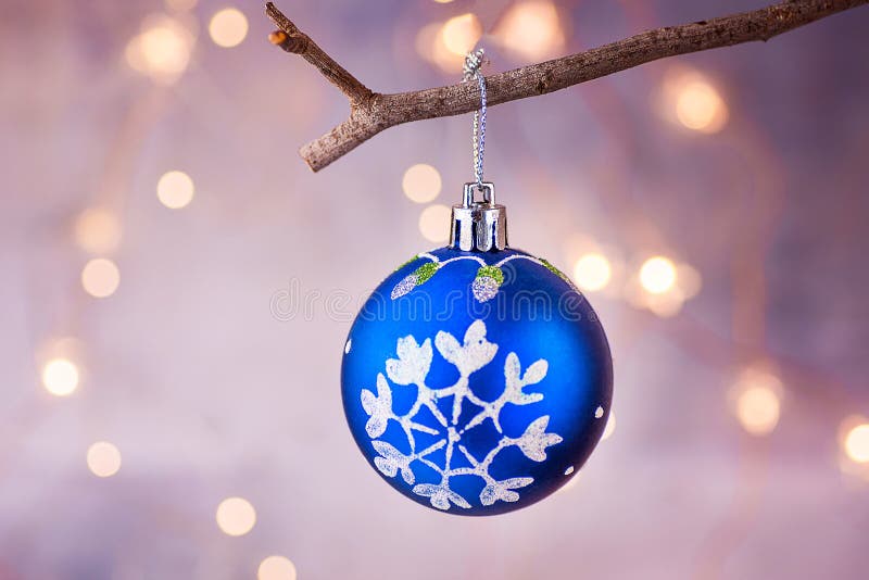 Blue Christmas tree ball with snow flake ornament hanging on branch. Shining garland golden lights.