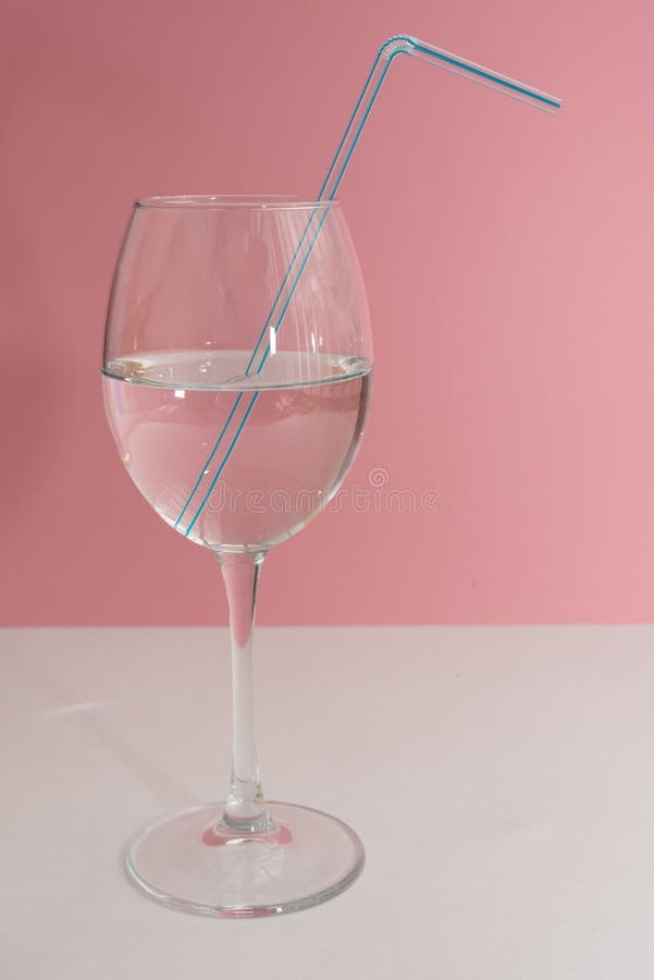 Blue drinking straw in the wine glass full with water on white table and pink background close up. Copy space, moc up stock image Blue drinking straw in the wine glass full with water on white table and pink background close up. Copy space, moc up stock image