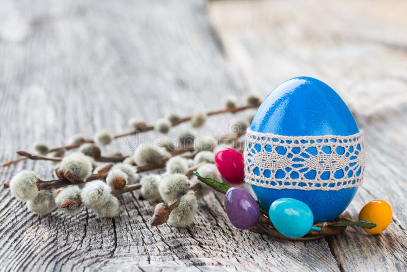 Blue Easter egg decorated with lace and willow branch on wooden background. Selective focus