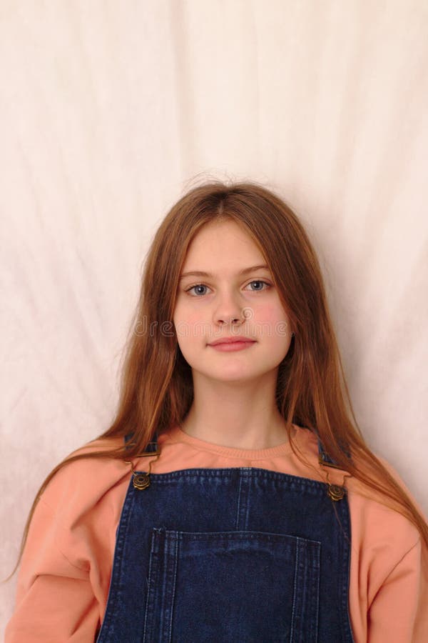 blue eyed brown haired shy girl in denim overalls. Studio model shot