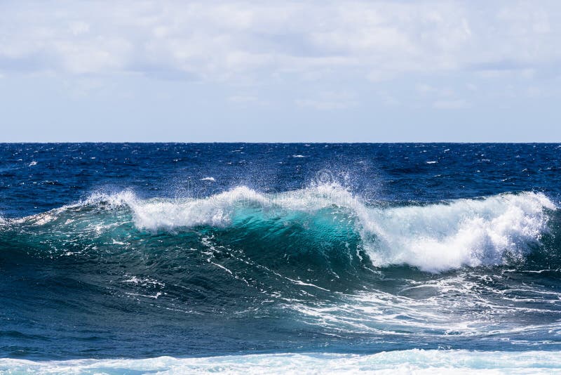 Blue-green wave breaking on Hawaii`s Big Island. Foam on top; deep blue Pacific ocean in background.