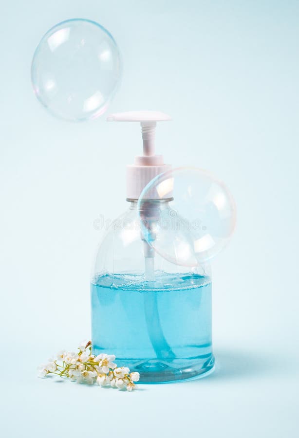 Blue Liquid Soap in Dispenser with Blooming Twig and Soap Bubbles on