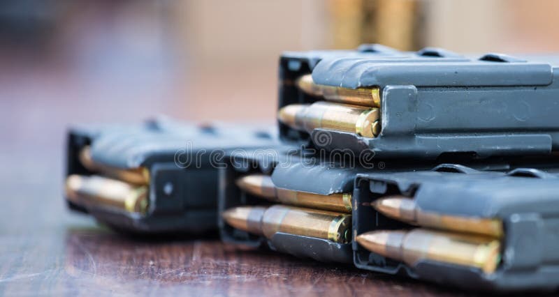 Magazines with bullets of firearm putted on wooden table. Close up view, blurred background.