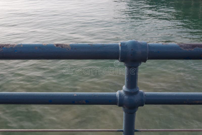 Blue metal railing with multiple layers of paint, viewed in front of green ocean water stock images