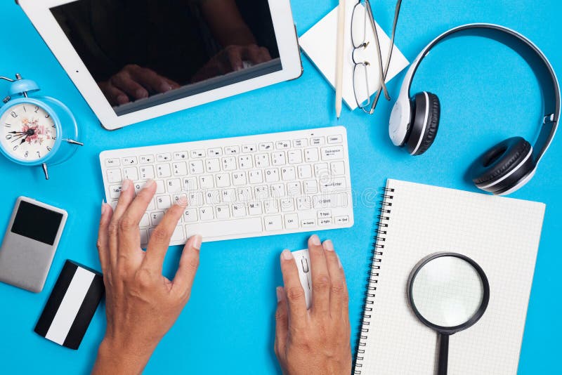 Blue office desk table with computer,wireless earphone,alarm clock and business objects, Top view for business background.