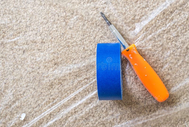 Blue painter`s tape and orange screwdriver on plastic covered carpet stock images Blue painter`s tape and orange screwdriver on plastic covered carpet stock images