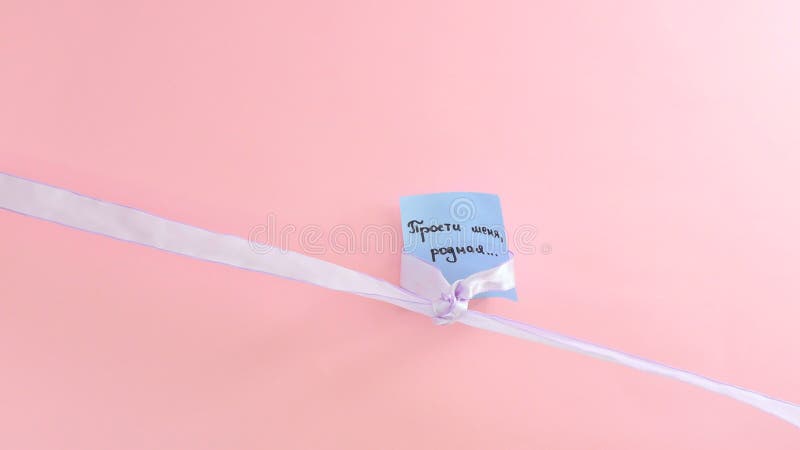 Blue ribbon tied in a bow on a piece of paper on pink background