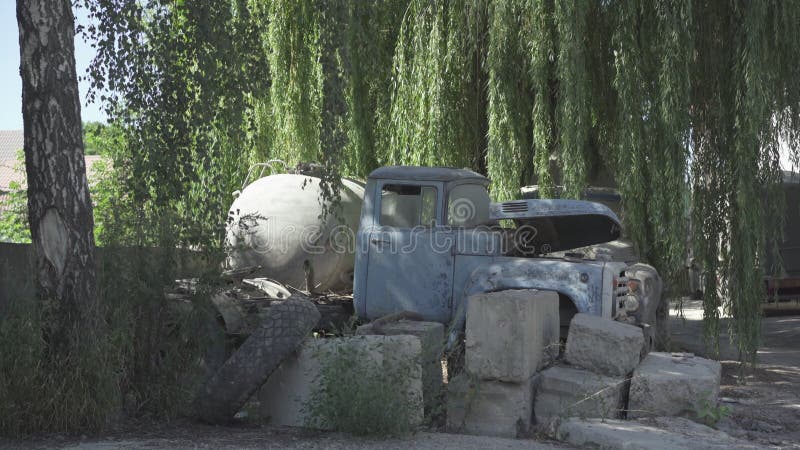 Blue rusty truck standing in sunlight on neglected production site. Abandoned machinery on former factory or plant