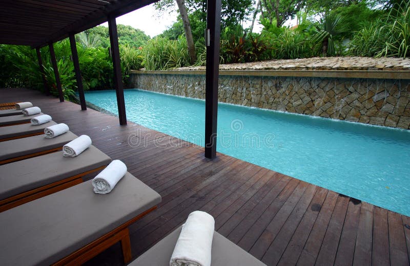 Un turchese blu resort offre una piscina all'aperto con riparo ponte di legno su un lato e lettini a bordo piscina in una riga.