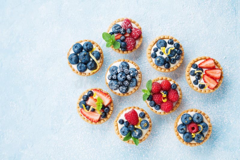 Blue table decorated of sugar powder with variety berry tartlets or cake top view. Tasty pastry desserts.