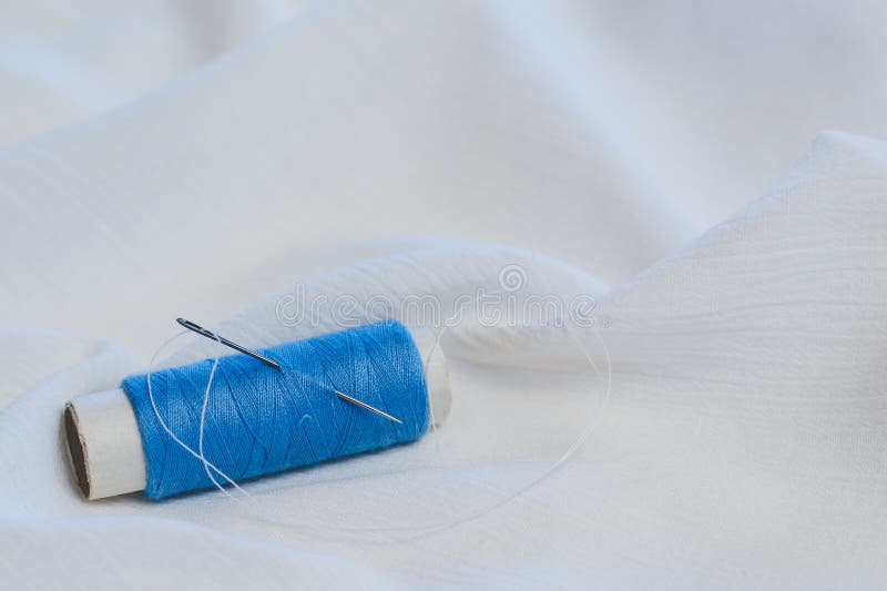 Blue Thread Spooll with Sewing Needle on White Cotton Cloth Stock Image