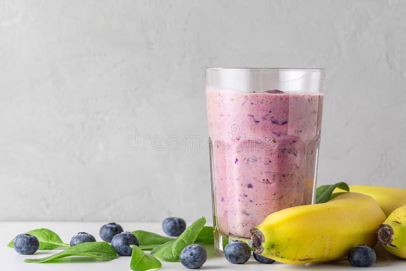 Blueberry, banana and spinach smoothie or milkshake in a glass with fresh fruits and berries. Healthy drink