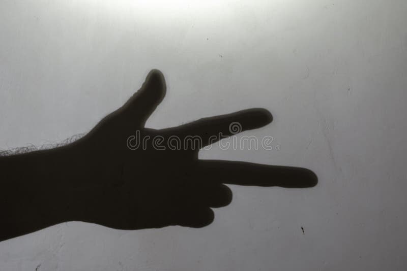 Blur, defocus, noise, grain effect. Dark silhouette of a hand showing a gesture from the fingers. Outline of a man`s hand with three fingers on a light gray wall. Selective focus