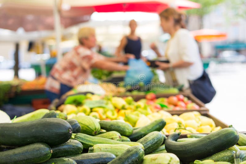 Blured unrecodnised people buying homegrown vegetable at farmers` market stall with variety of organic vegetable.