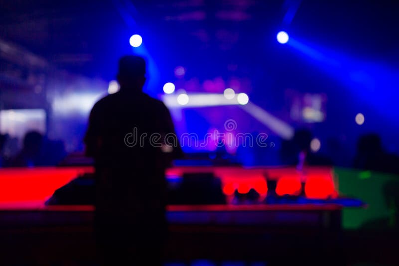 Blurred background : Club, disco DJ playing and mixing music for crowd of happy people. Nightlife, concert lights