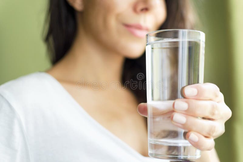 Blurred girl in a white T-shirt holding a glass with water and smiles. Green background royalty free stock photo Blurred girl in a white T-shirt holding a glass with water and smiles. Green background royalty free stock photo