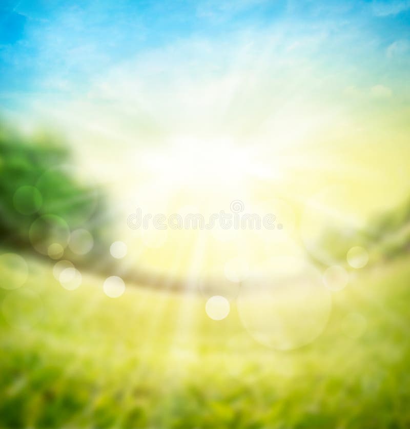 Blurred spring summer nature background with green meadow, trees on horizon and sun rays