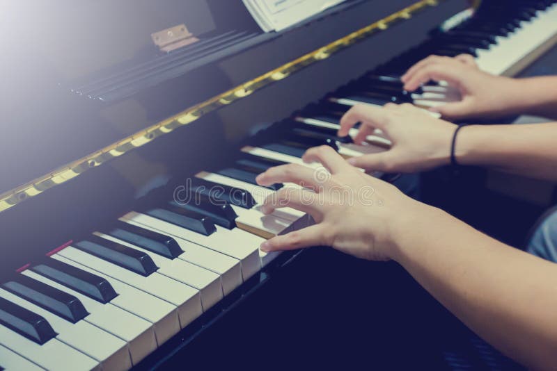 Blurry fingers of young woman and a boy pressing key to play the piano with music notation